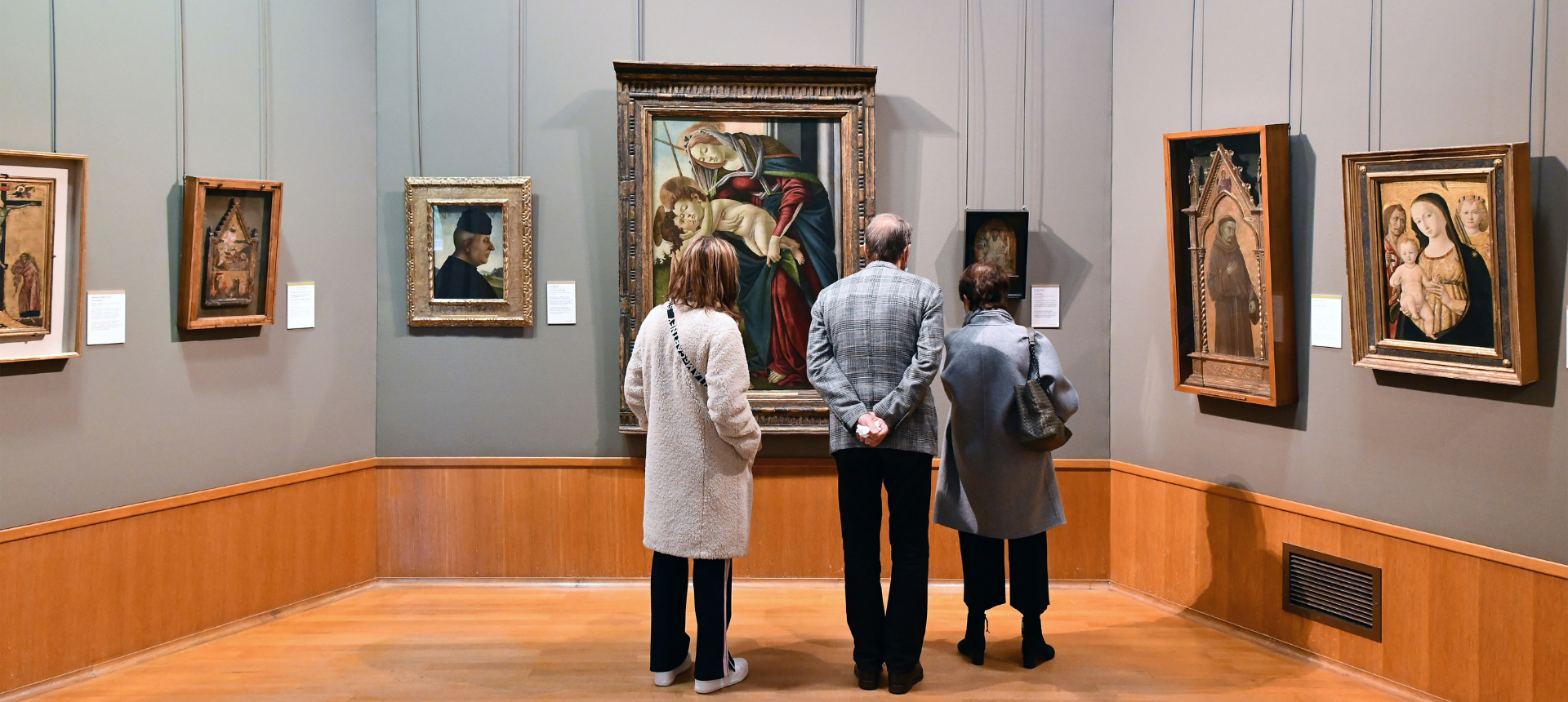 Three people shown from behind looking intently at an artwork in a gallery