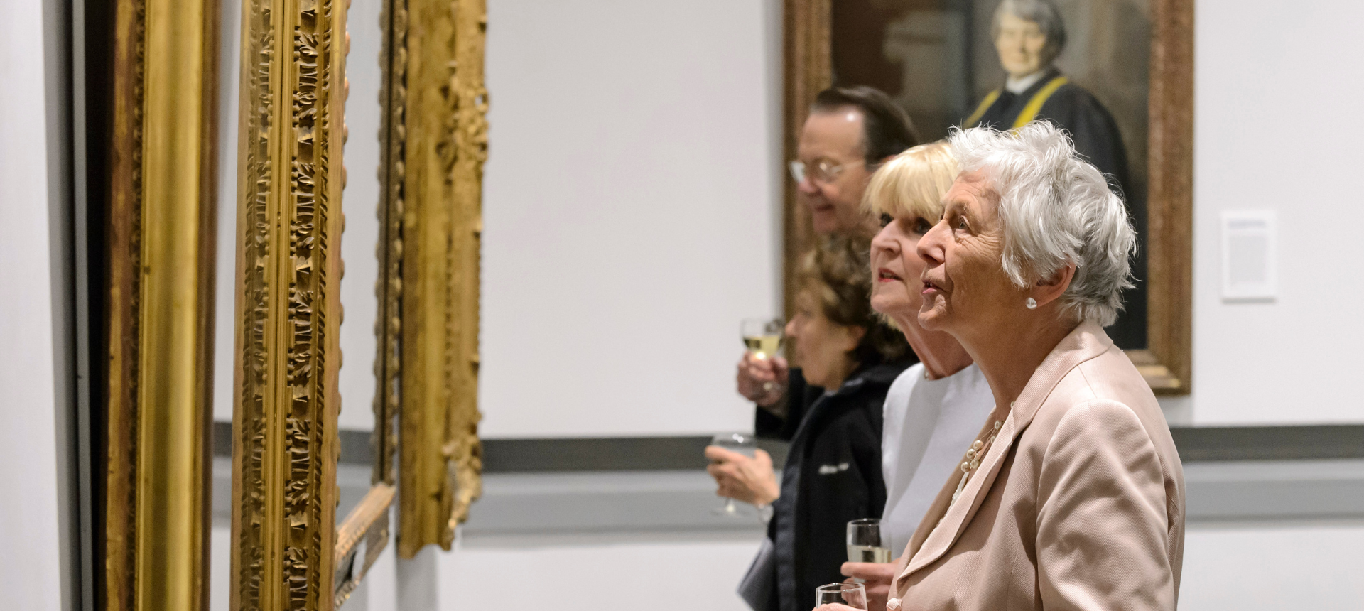Several people looking at artworks, some holding wine glasses.