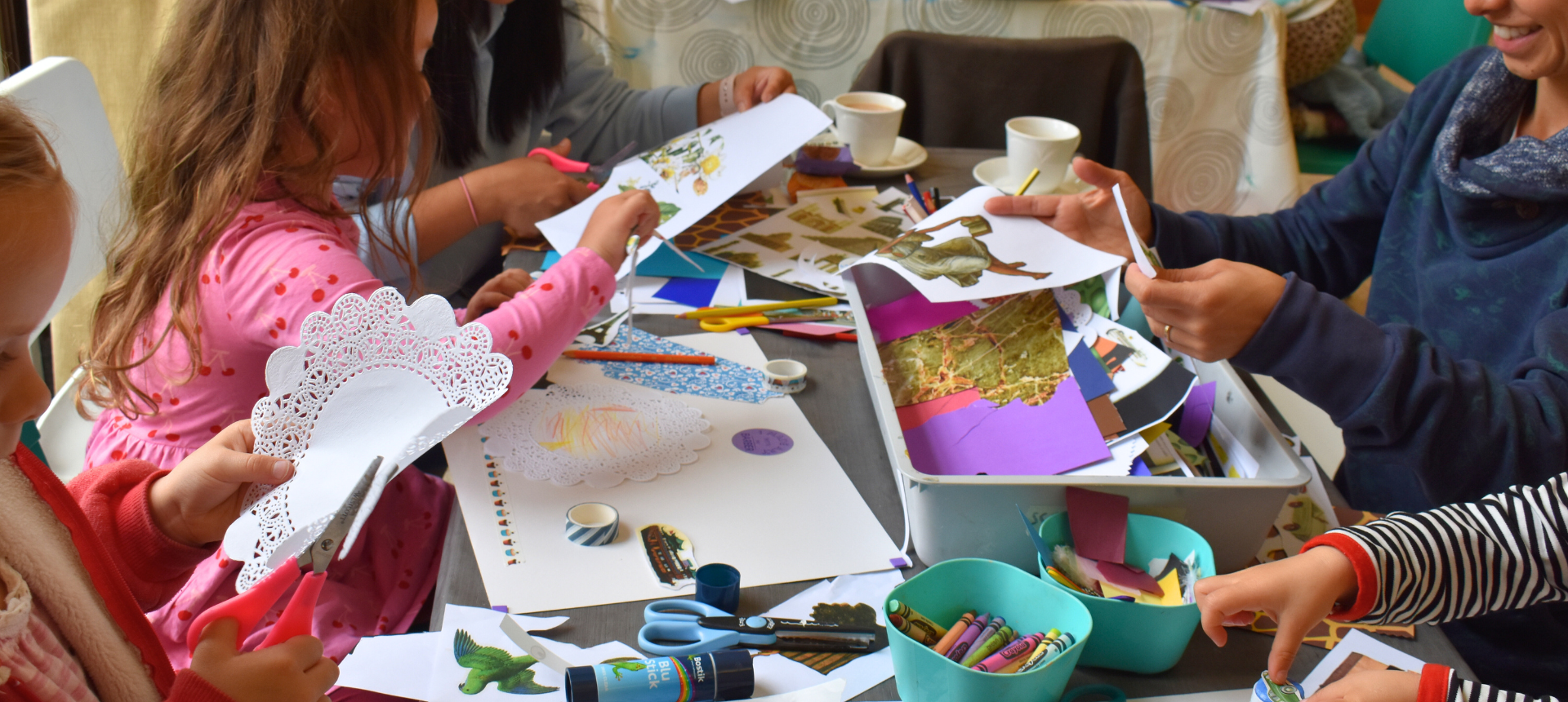 Craft supplies on a table, children's hands can be seen cutting and sticking.
