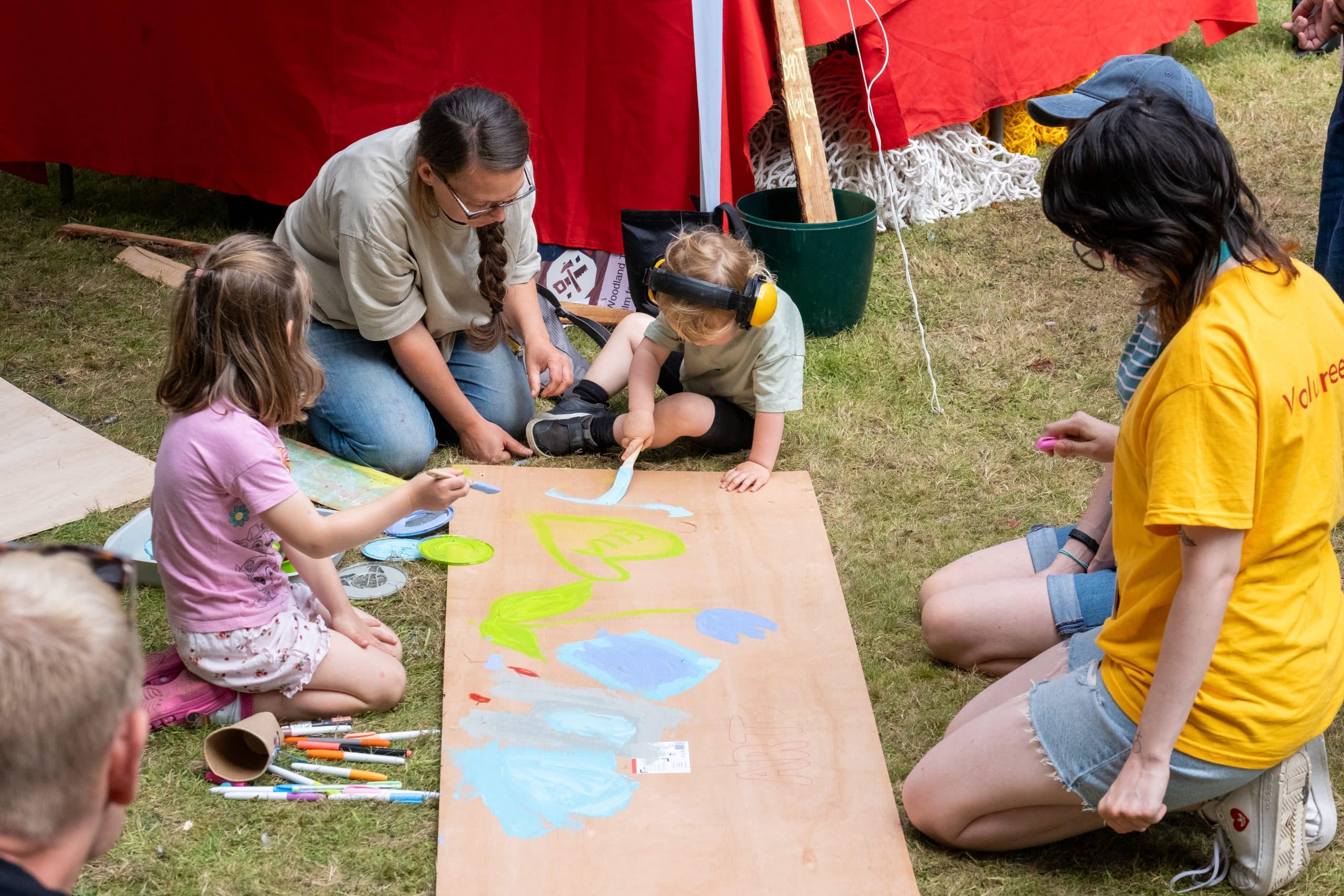 children drawing with bright colours, outdoors on a long piece of wood.