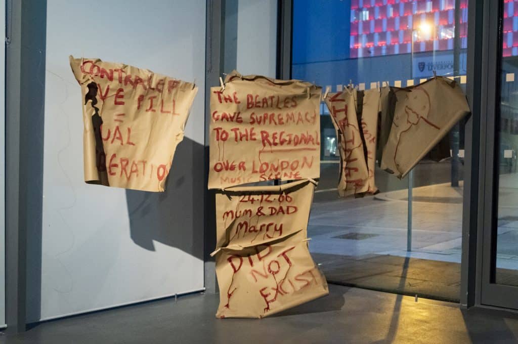An installation of collaborative artwork, with red writing on brown cardboard.